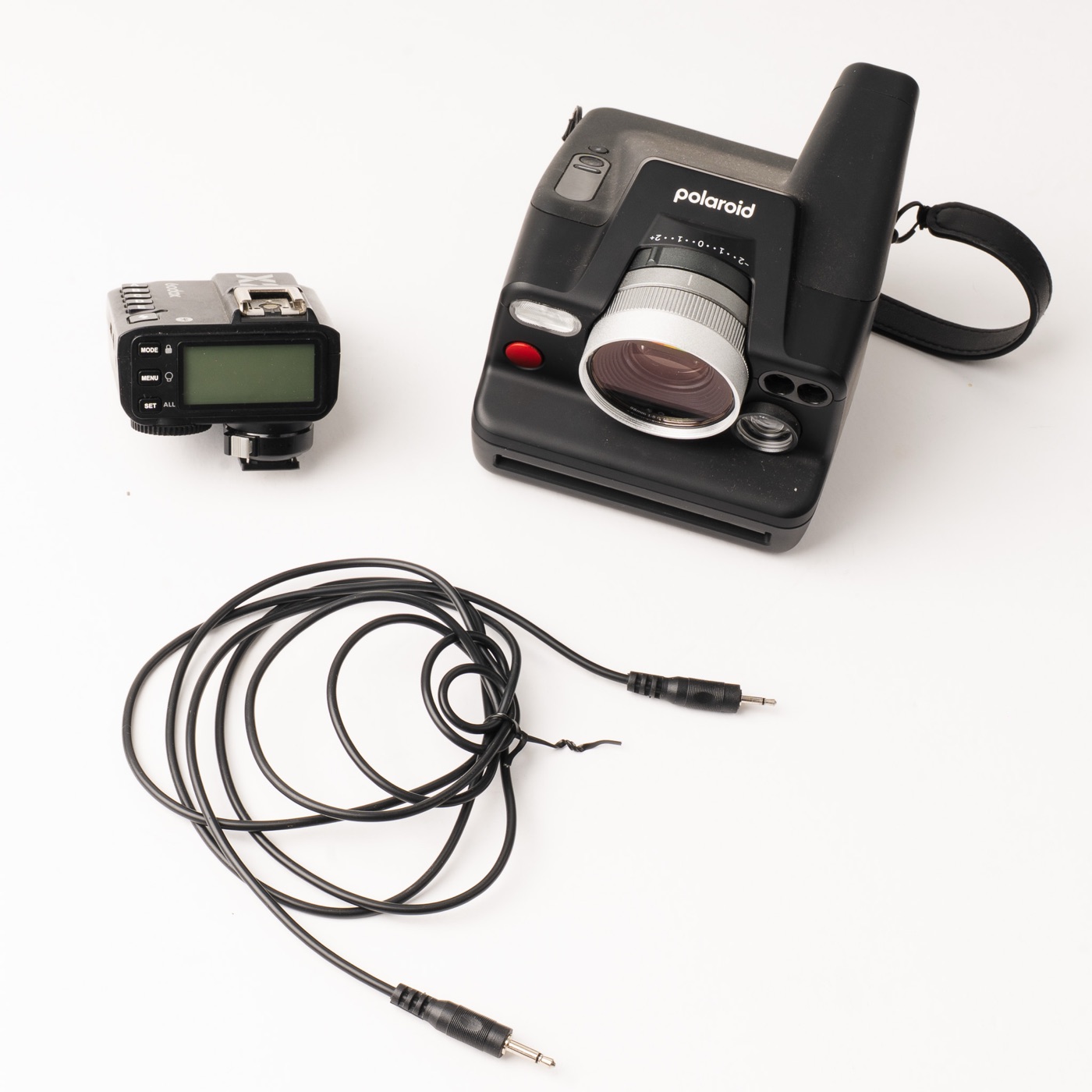Polaroid I-2, a Godox X2T flash trigger and a two-ended sync cable laid out on white