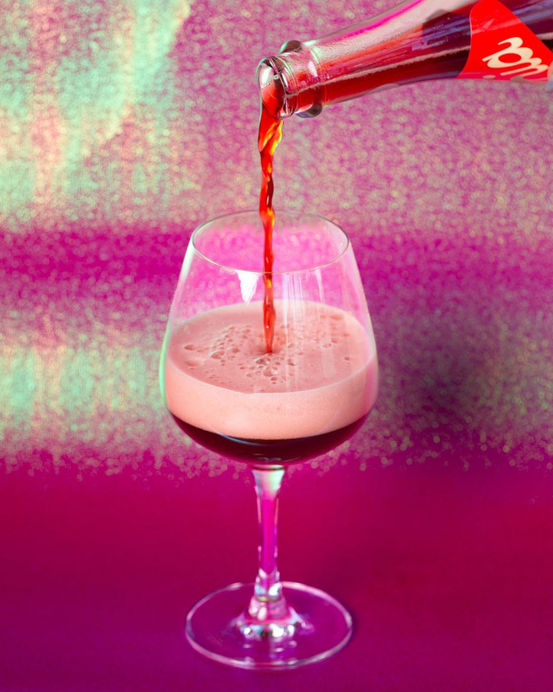 Red drink pouring into a glass on iridescent pink