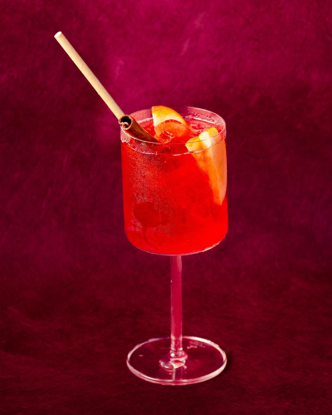 Red cocktail with cinnamon and apple on deep red